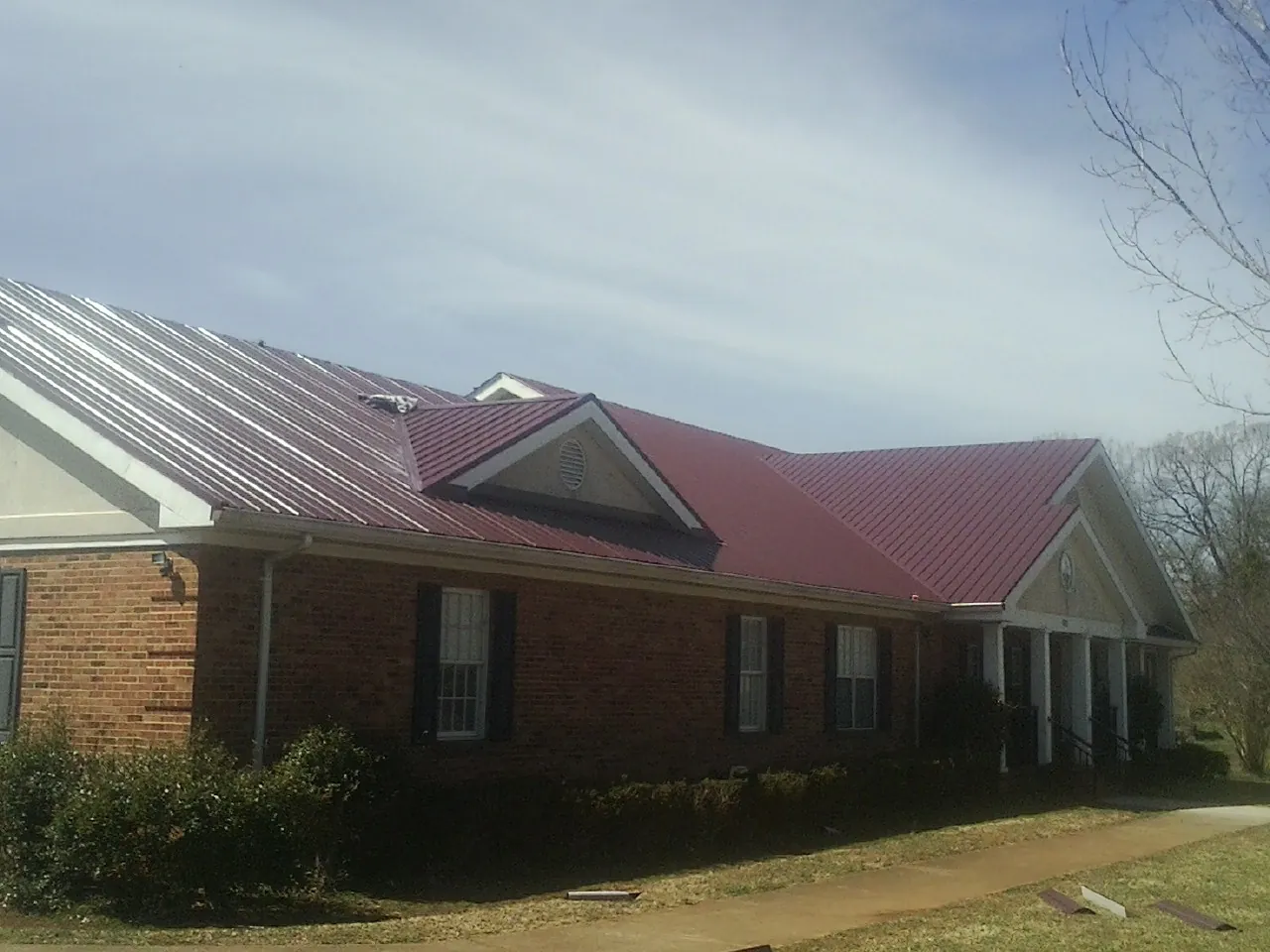 Red metal roof with gabled entries on a long brick building, from a Hail Damage Roof Repair job in Armstrong Creek