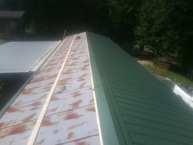 Old rusted panels beside newly installed green metal roofing — Wind Damage Roof Repair by Roofing Brothers in Armstrong Creek