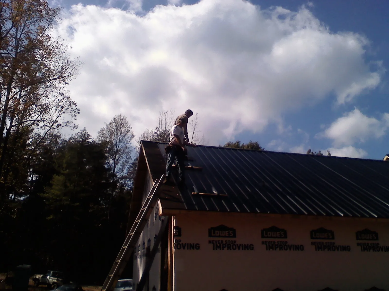 Roofer fastening dark metal panels high against a cloudy sky, from a Roof Inspection job in Armstrong Creek
