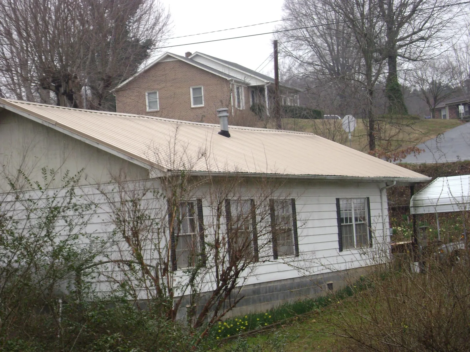 Tan metal roof on a white sided house set into a hillside — Commercial Roofing by Roofing Brothers in Armstrong Creek