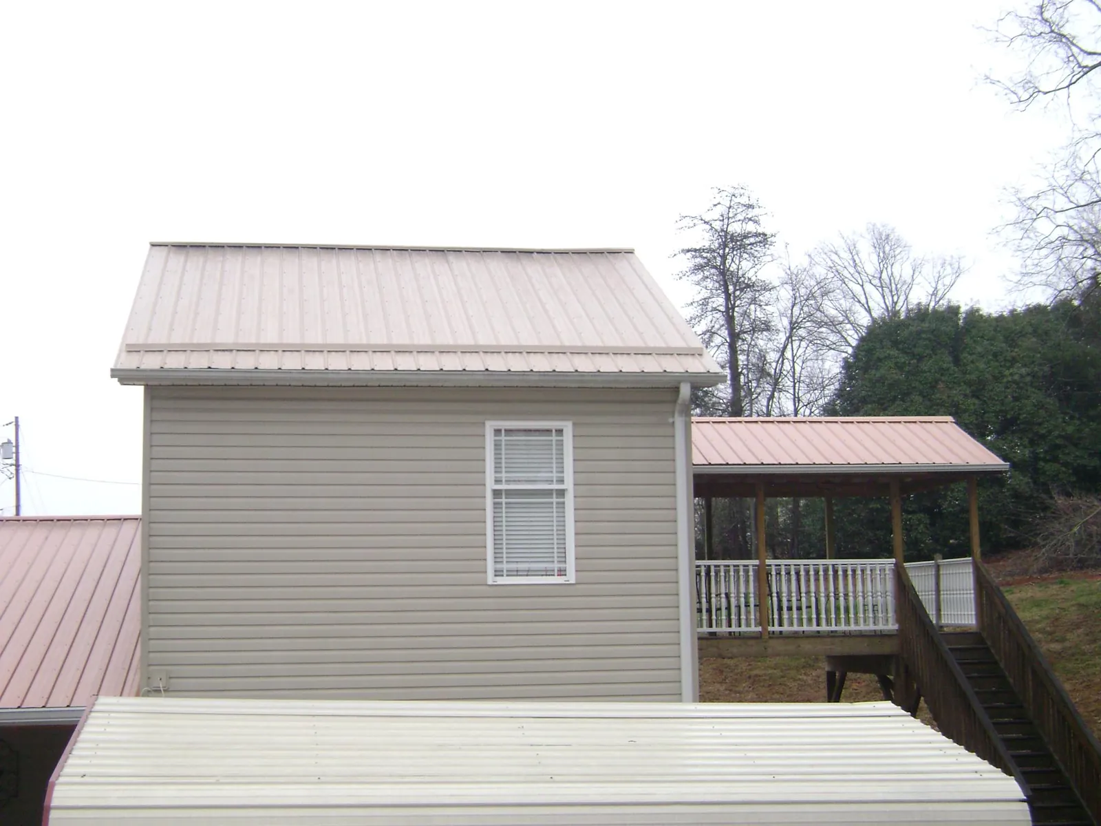 Tan metal roofs on a two story addition and attached porch, from a Roof Replacement job in Armstrong Creek